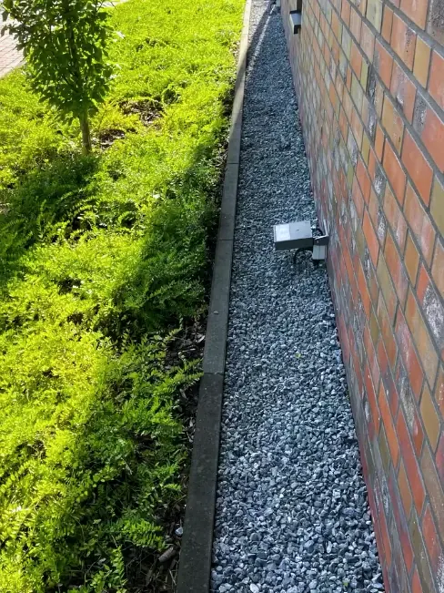Kiesstreifen zwischen Klinkerwand und Beet nach der Arbeit: der Kies liegt frei, der Randstein ist wieder sichtbar, aus dem Streifen wächst nichts mehr heraus